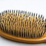 Image en gros plan d'une brosse à cheveux en poils de sanglier, détaillant la texture réaliste des poils, sur un fond blanc minimaliste.